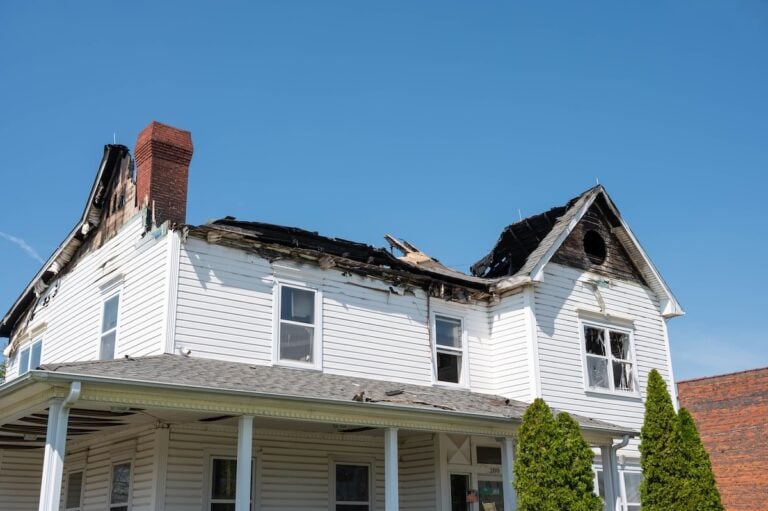 The burned house has roof damage. The windows are broken on the fire damaged house.