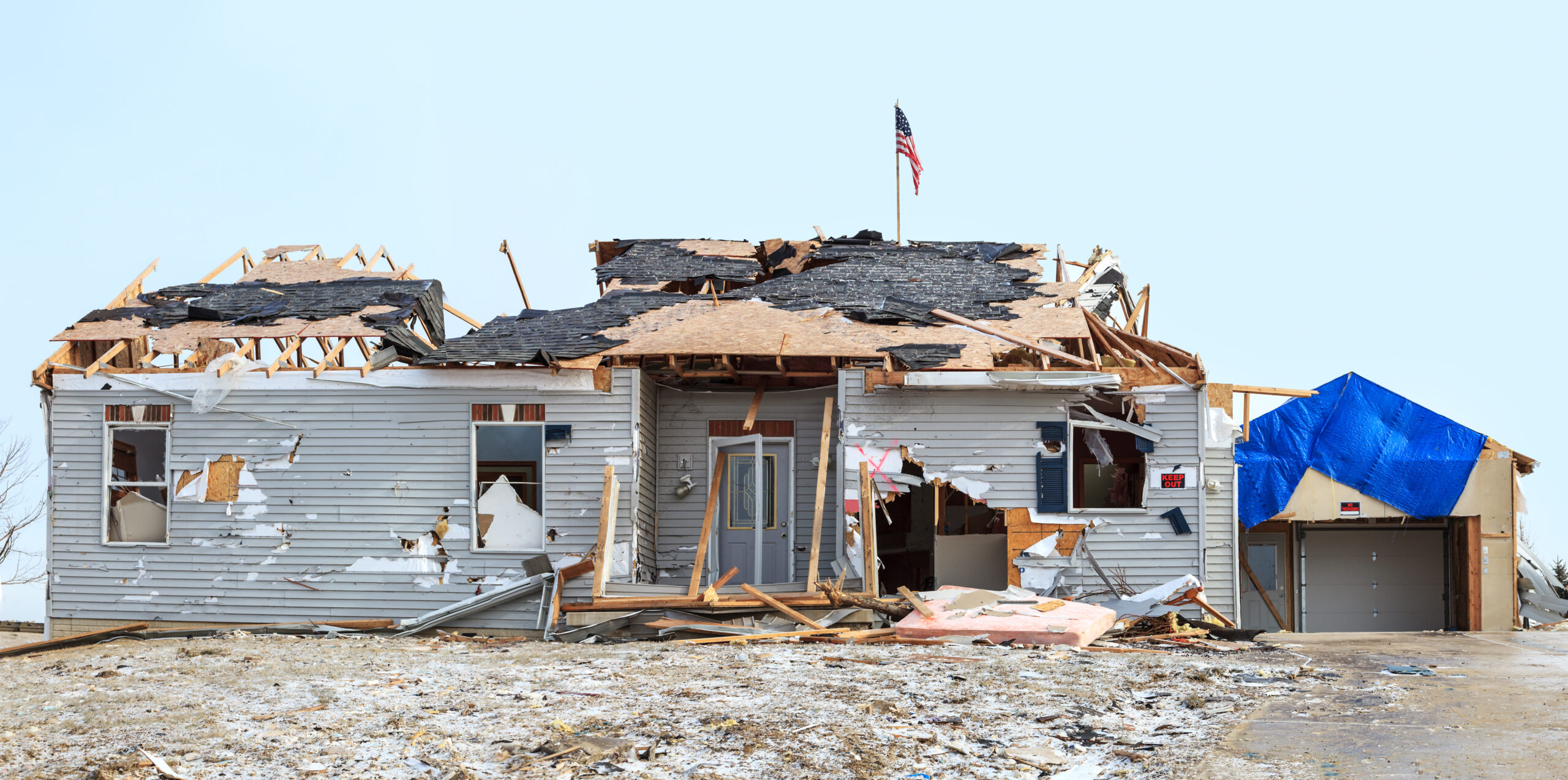 A home destroyed by a tornado with the USA flag in the background.