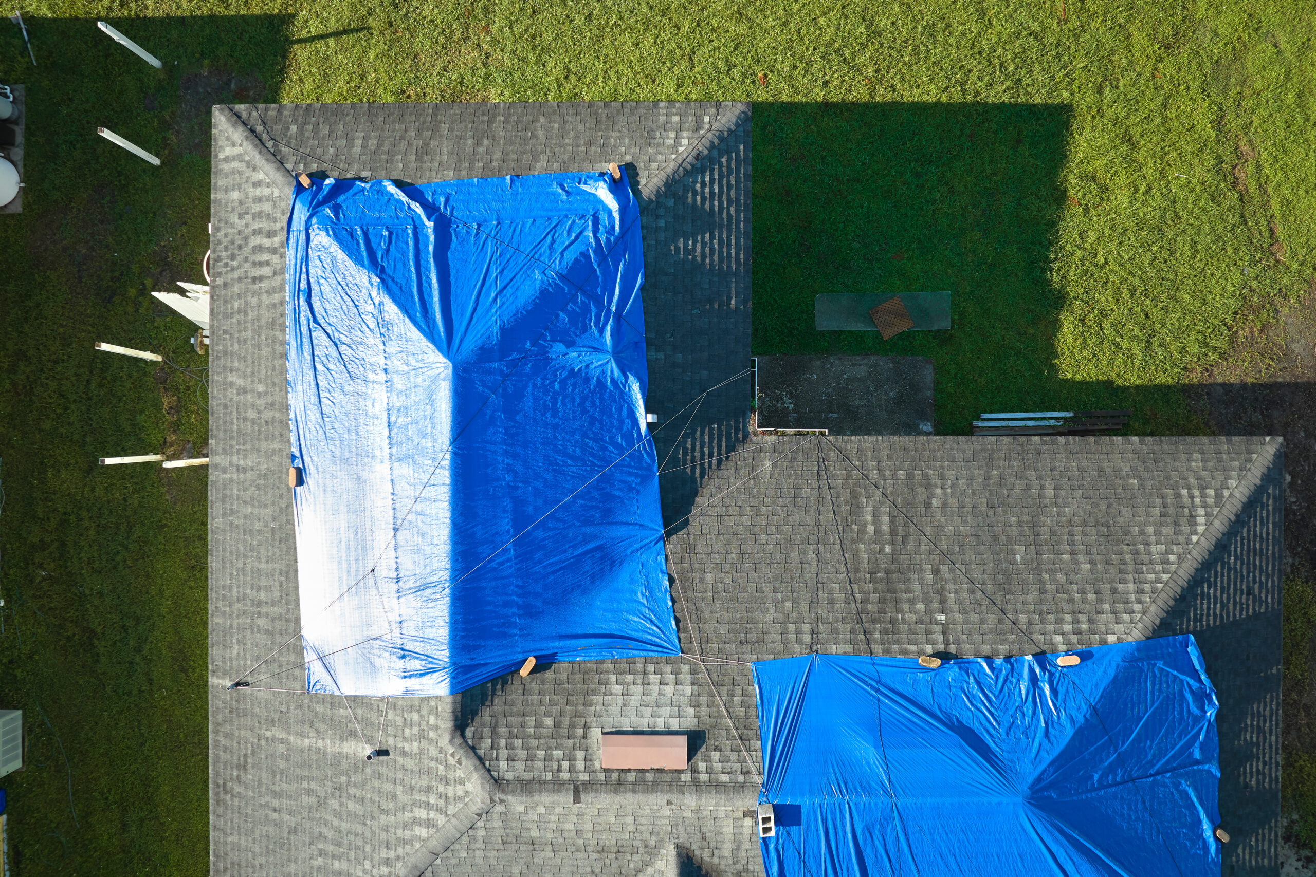Top view of leaking house roof covered with protective tarp sheets against rain water leaks until replacement of asphalt shingles. Damage of building rooftop as aftermath of hurricane Ian in Florida.